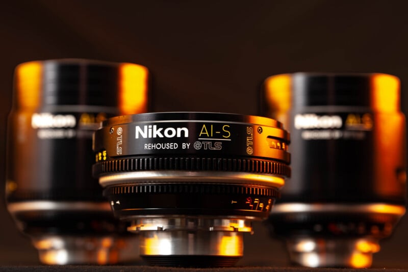 Three Nikon AI-S lenses rehoused by TLS are arranged on a dark surface, with the center lens in sharp focus.