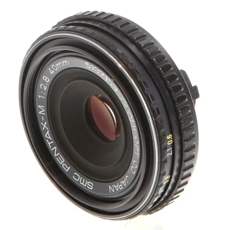 An SMC Pentax-M 40mm f/2.8 pancake lens shown at an angle against a white background.