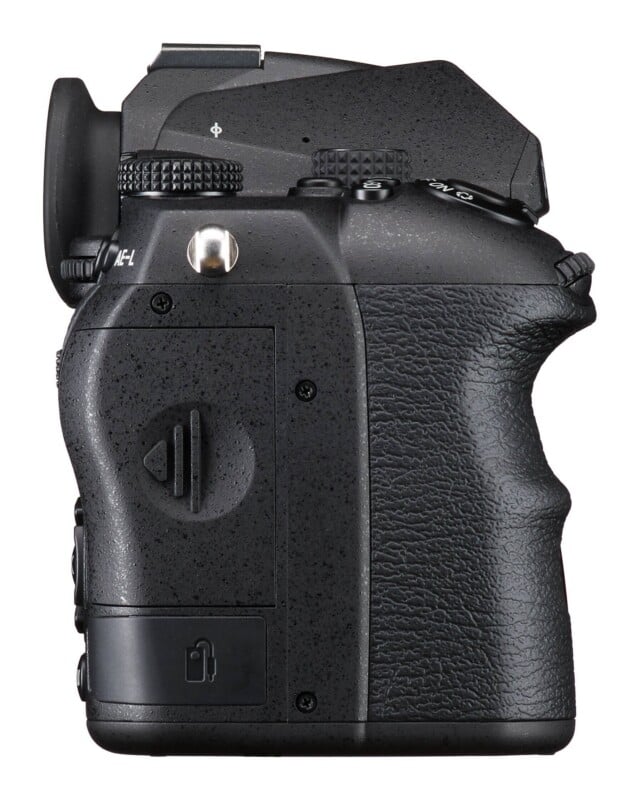 A side view of a black digital camera body showing the textured grip, a memory card slot door, and various control dials and buttons.