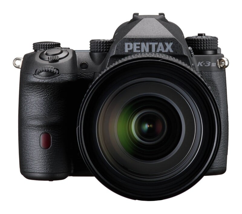 A black Pentax K-3 III DSLR camera with a large lens attached, shown from a front-facing perspective against a white background.