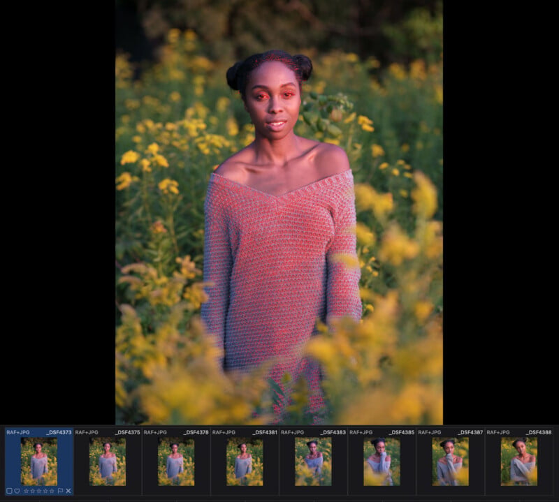 A woman with space buns stands in a field of yellow flowers, wearing an off-the-shoulder sweater illuminated by warm light.