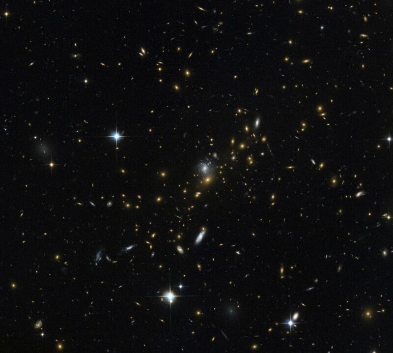 A dense field of distant galaxies of various shapes and sizes, interspersed with several bright, spiked foreground stars.