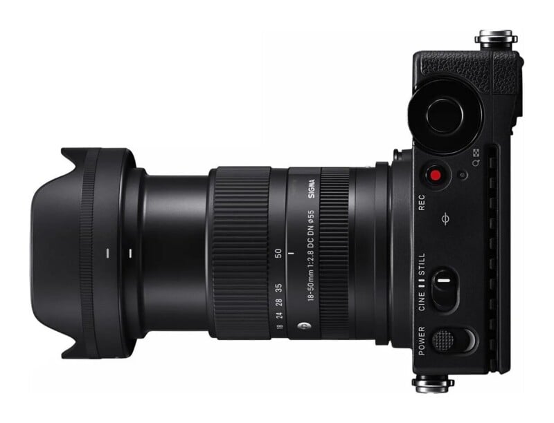 A top-down view of a black mirrorless camera with a Sigma 18-50mm f/2.8 lens attached, showing the power switch, mode selector, and record button.