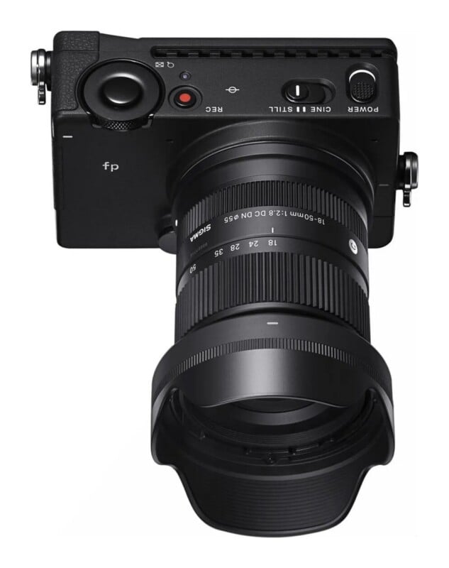 A top-down view of a black digital camera with a Sigma 18-50mm lens attached, showing the power switch, record button, and mode toggle.
