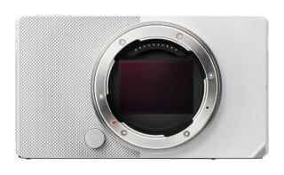 A front-facing silver digital camera body with an exposed sensor and lens mount, featuring a textured grip on the left side.
