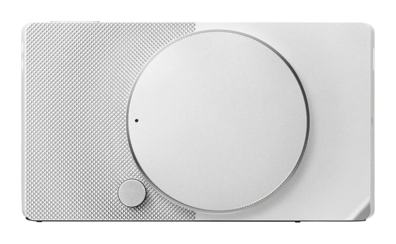 A rectangular silver device with a textured, diamond-patterned left side, a large circular dial in the center, and a small circular button below the dial.