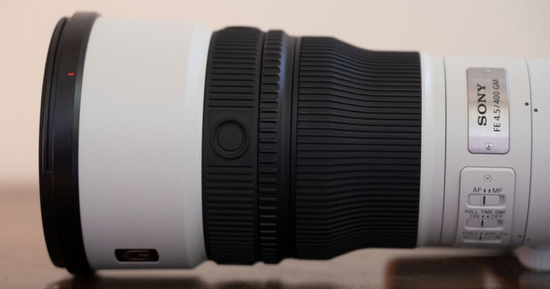 A close-up side view of a white Sony FE 4.5/400 GM telephoto lens, showing the focus ring, function button, and control switches on the barrel.