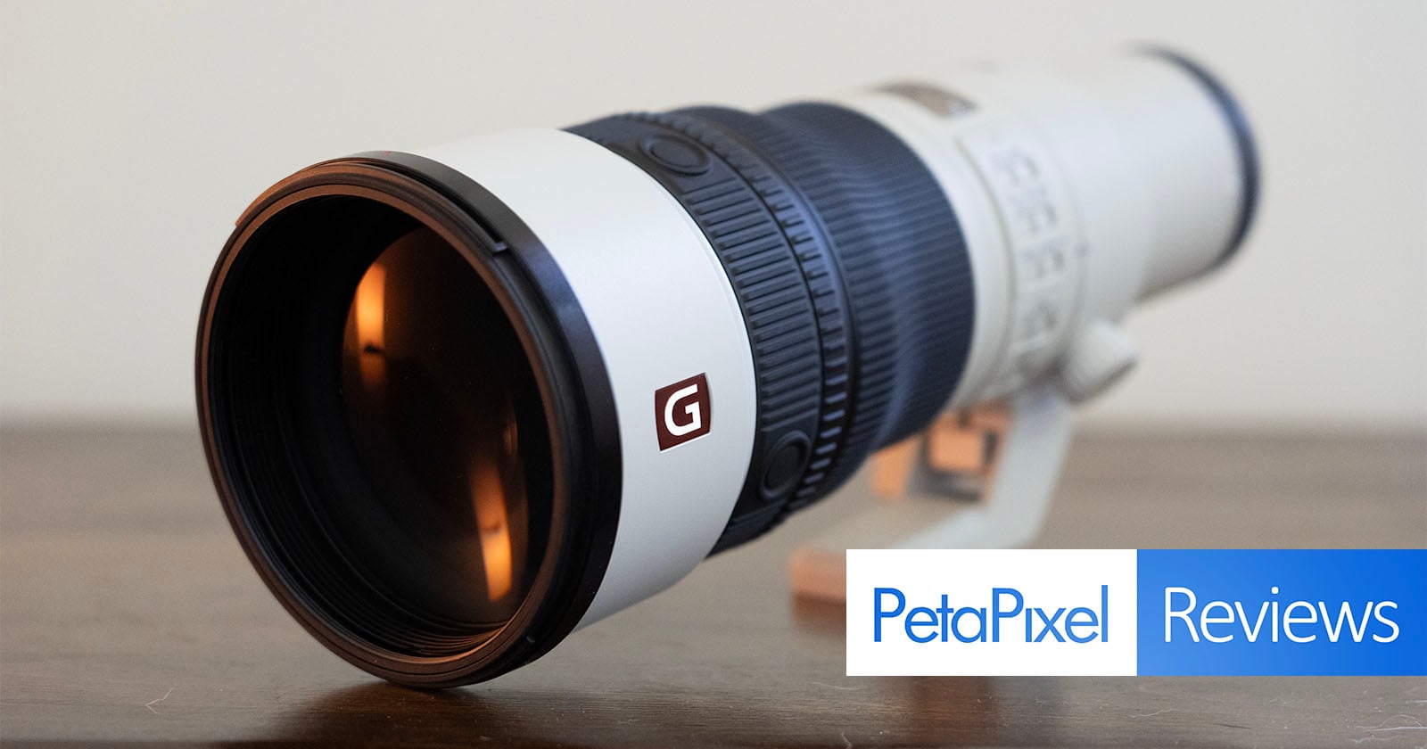A white telephoto camera lens with a prominent "G" logo sits on a wooden surface, with a PetaPixel Reviews logo in the corner.