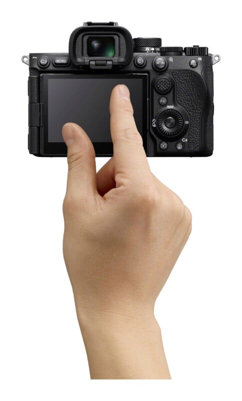 A hand holds a digital camera, with the index finger touching the back screen.