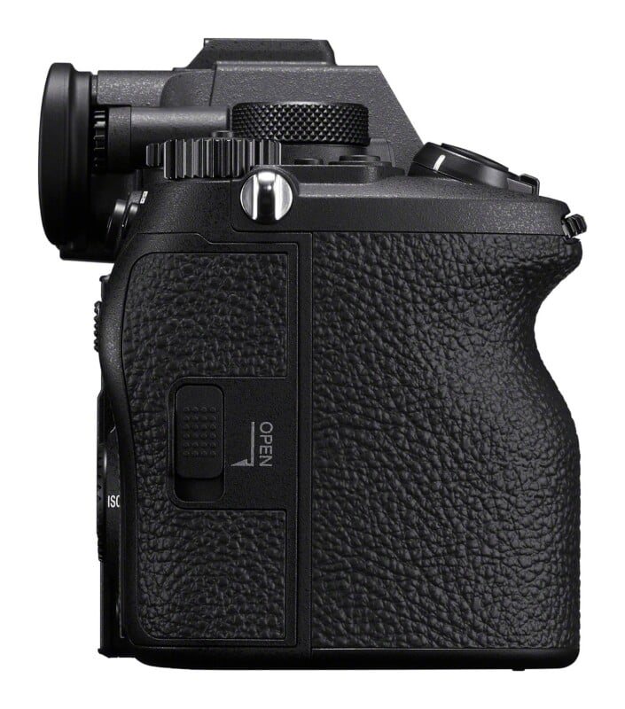 A side view of a black digital camera body showing the textured hand grip, a strap lug, and a side door labeled "OPEN.