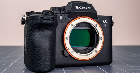 A black Sony Alpha 7 mirrorless camera body with an E-mount lens opening sits on a gray cutting mat.