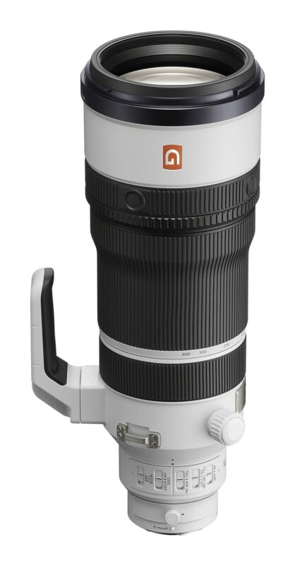 A white and black telephoto zoom lens for a camera, shown from a side angle, featuring a large focus ring, a tripod mount, and various control switches on the base.
