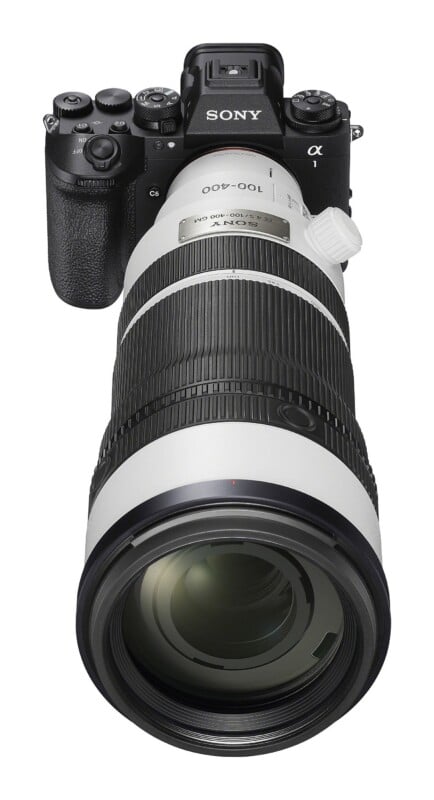 A Sony Alpha camera with a large white telephoto zoom lens attached, viewed from a top-down angle against a white background.