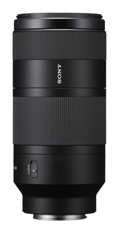 A black Sony telephoto camera lens standing vertically against a white background, featuring a zoom ring and a focus lock switch.