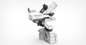 A white camera rig featuring a top handle, a battery mount, and an electronic viewfinder attached to a camera body on a white background.