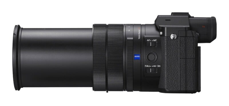 A side view of a black digital camera with a long zoom lens, featuring a Zeiss logo and focus switches on the barrel.