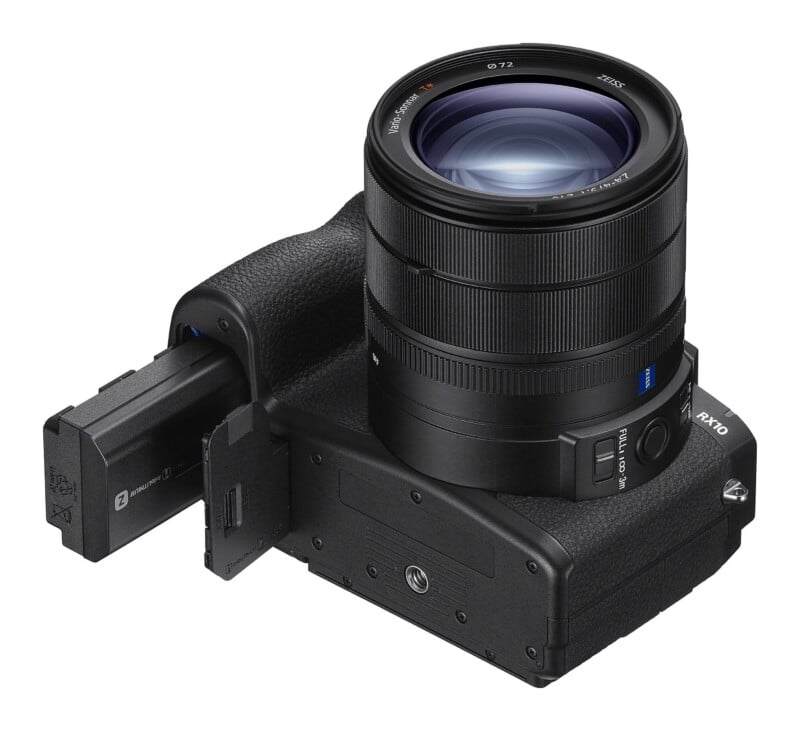 A black digital camera viewed from the bottom, with its battery compartment door open and a rectangular battery partially inserted.