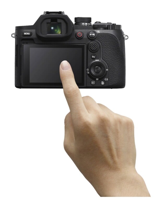 A hand points a finger at the blank LCD screen of a black digital camera.