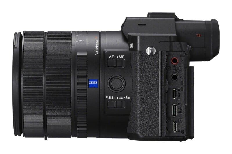 Side view of a black digital camera with a large lens, showing focus switches, a Zeiss logo, and a panel of open ports including HDMI, USB, and audio jacks.