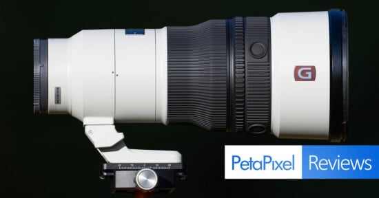A white telephoto camera lens mounted on a tripod head against a black background, with a PetaPixel Reviews logo in the corner.