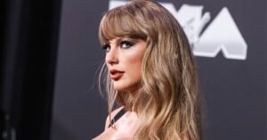 Taylor Swift with blonde hair and bangs looks over her shoulder at the camera against a dark background with partial text.