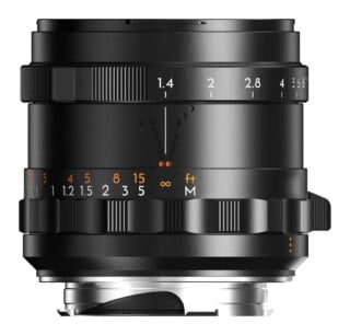 A black manual focus camera lens shown from the side, featuring an aperture ring with f-stops from 1.4 to 8 and a focus ring with distance markings in feet and meters.