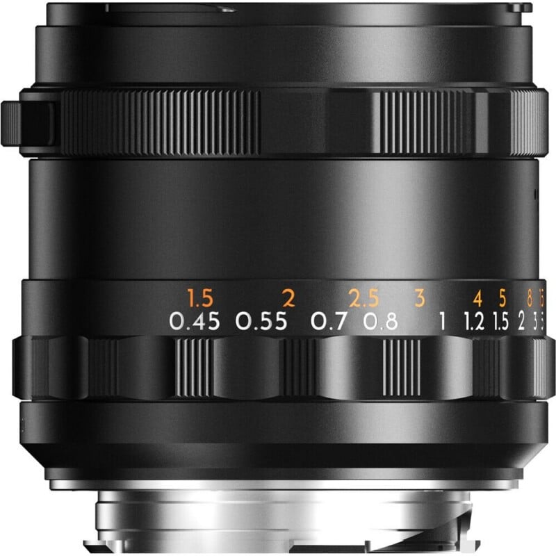 A black camera lens barrel featuring a focus ring with orange and white distance markings in feet and meters.