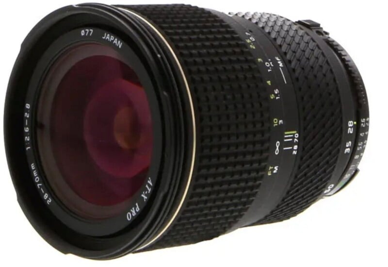 A black Tokina AT-X PRO 28-70mm f/2.6-2.8 camera lens with a 77mm filter thread, shown from a side-angled perspective.