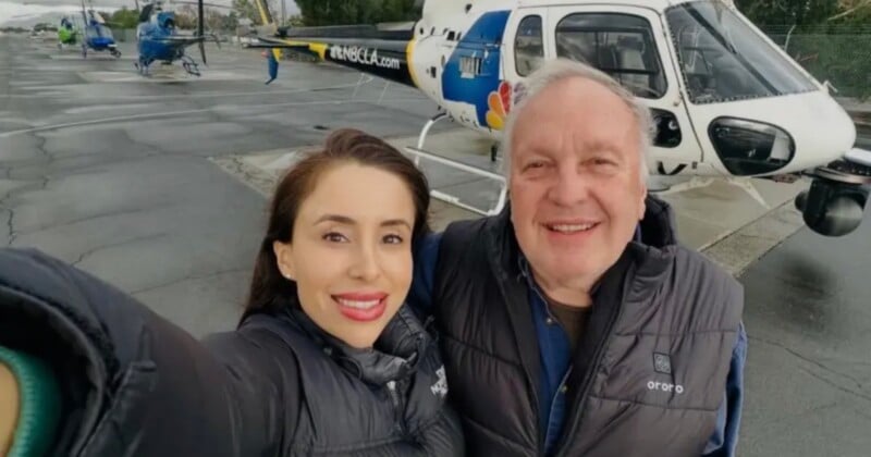 A woman and an older man take a selfie together in front of an NBCLA news helicopter parked on an airfield.