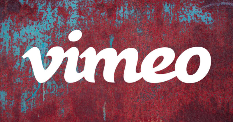 The white Vimeo logo is centered over a background of weathered, rusted metal with patches of blue paint.