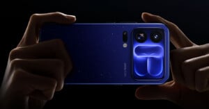 A pair of hands holds a dark blue smartphone with a starry pattern on the back and a prominent camera module featuring two large lenses and a distinct, glowing blue geometric design.