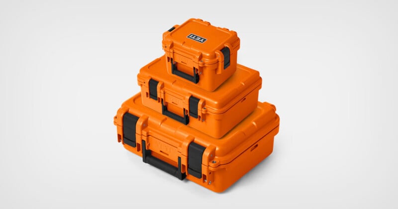 Three bright orange YETI hard-shell storage cases stacked on top of each other against a plain light gray background.