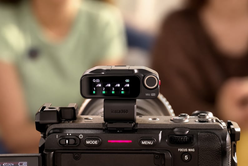 An Insta360 wireless microphone receiver is mounted on top of a camera, displaying signal levels for four channels on its screen.