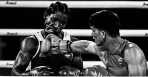 A black-and-white action shot of a boxer landing a punch on his opponent's face during a match.