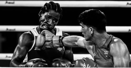 A black-and-white action shot of a boxer landing a punch on his opponent's face during a match.