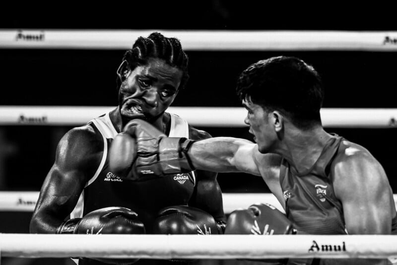 A black-and-white action shot of a boxer landing a punch on his opponent's face during a match.