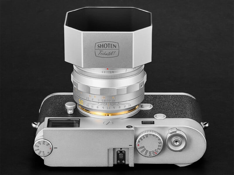 A silver rangefinder camera with a silver lens and a square metal lens hood, viewed from above against a black background.