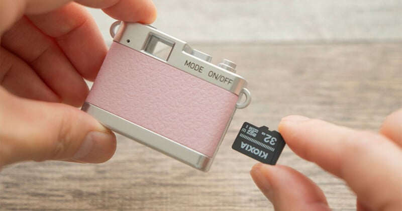 A person holds a small, pink and silver toy-like camera in one hand and a Kioxia 32GB microSD card in the other.