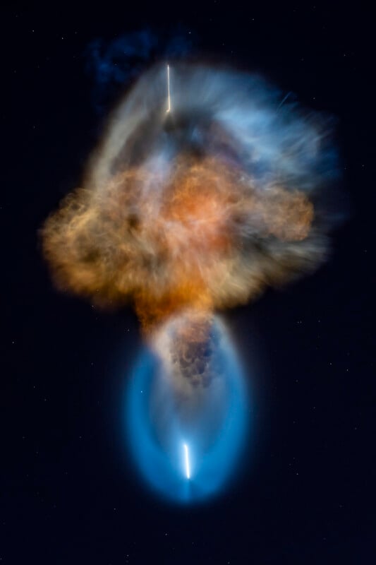 A bright rocket plume creates a large, glowing blue and orange nebula-like cloud against a dark, starry night sky.