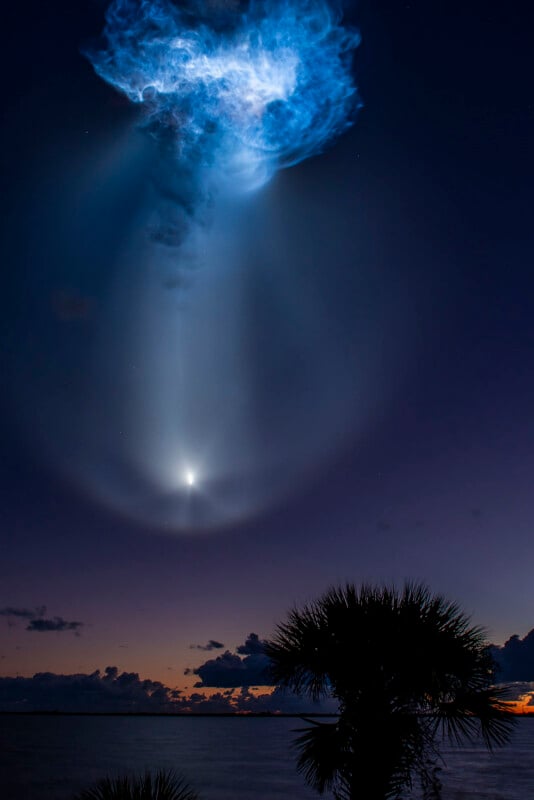 Large circular glow created by a rocket exhaust plume fills the predawn sky above the horizon.