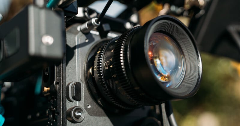 A close-up view of a professional cinema camera lens with a focus ring marked "100 T1.9" and a button labeled "GRAB" on the camera body.