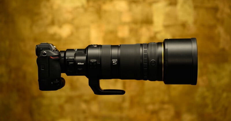 A side view of a Nikon Z-series mirrorless camera attached to a large telephoto Nikkor S lens against a textured gold background.