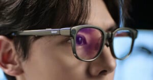 A close-up side view of a person wearing dark-rimmed glasses with the word "Qwen" printed on the temple.