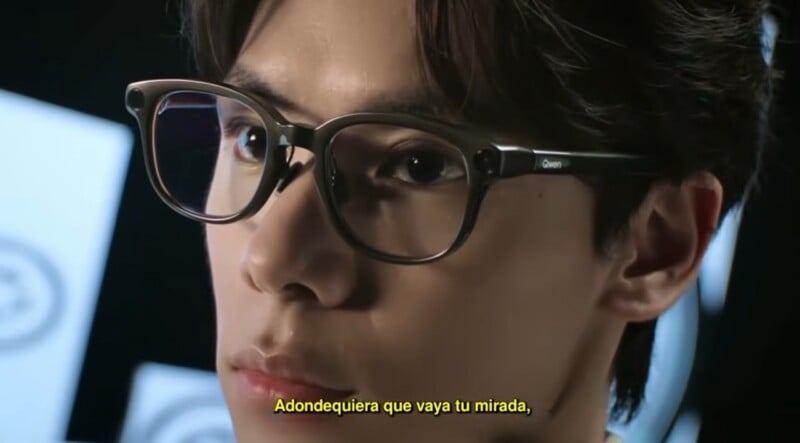 A close-up shot of a person wearing dark-rimmed glasses with the word "Qwen" printed on the temple, with Spanish subtitles at the bottom.