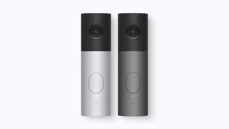 Two vertical, cylindrical smart doorbells stand side-by-side against a white background, one in silver and one in dark gray.