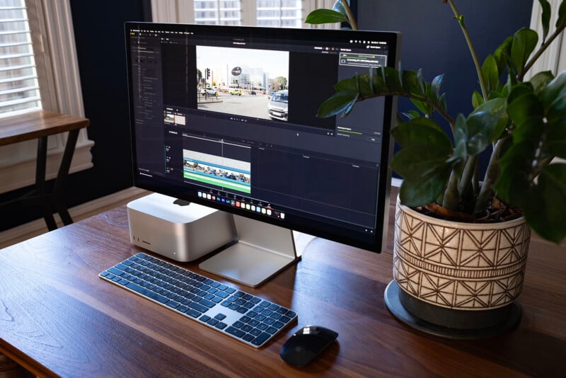A desktop computer setup with a monitor, keyboard, and mouse on a wooden desk next to a potted plant.