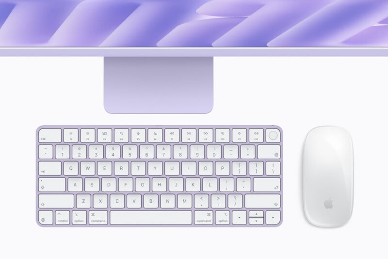 A purple iMac computer with a matching wireless keyboard and a white Magic Mouse on a white surface.