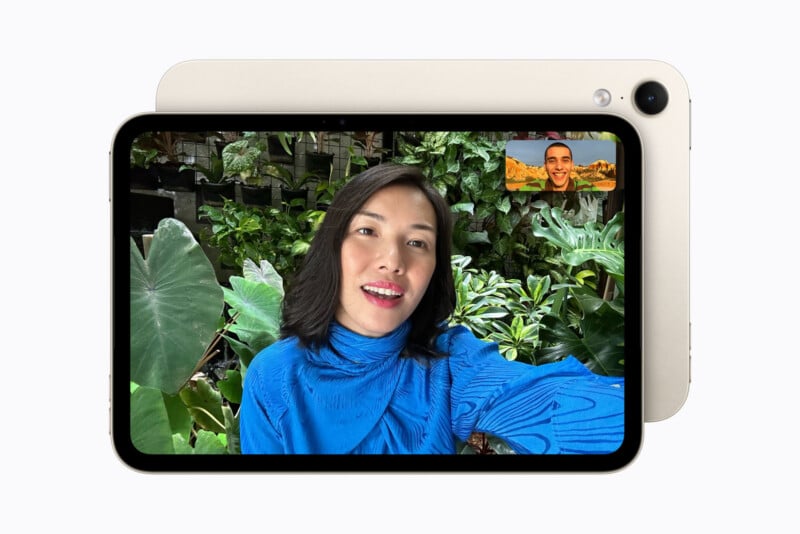 A tablet displays a video call between a woman in a blue top and a man in a small inset window, with a light-colored tablet casing visible behind the screen.