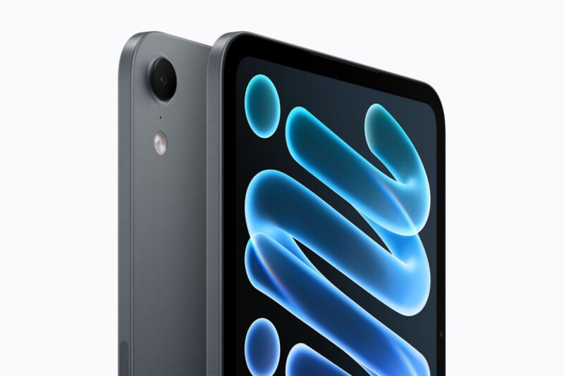 A close-up view of a dark gray tablet showing its rear camera lens, flash, and a portion of its screen displaying a blue abstract graphic.