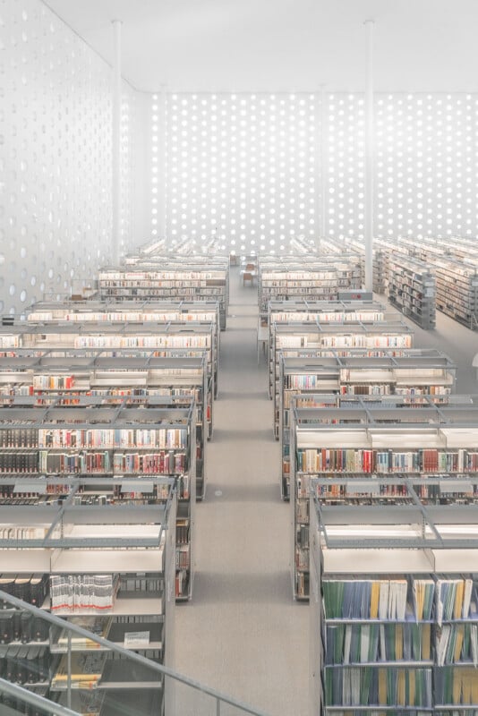 Rows of tall, metal bookshelves filled with books in a bright, minimalist library featuring walls with a repeating circular pattern.